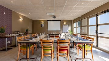 A conference room with multiple tables and chairs, a projector screen, and large windows.