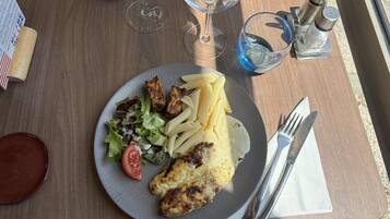 Un plato con pollo a la plancha, pasta y ensalada sobre una mesa de madera.