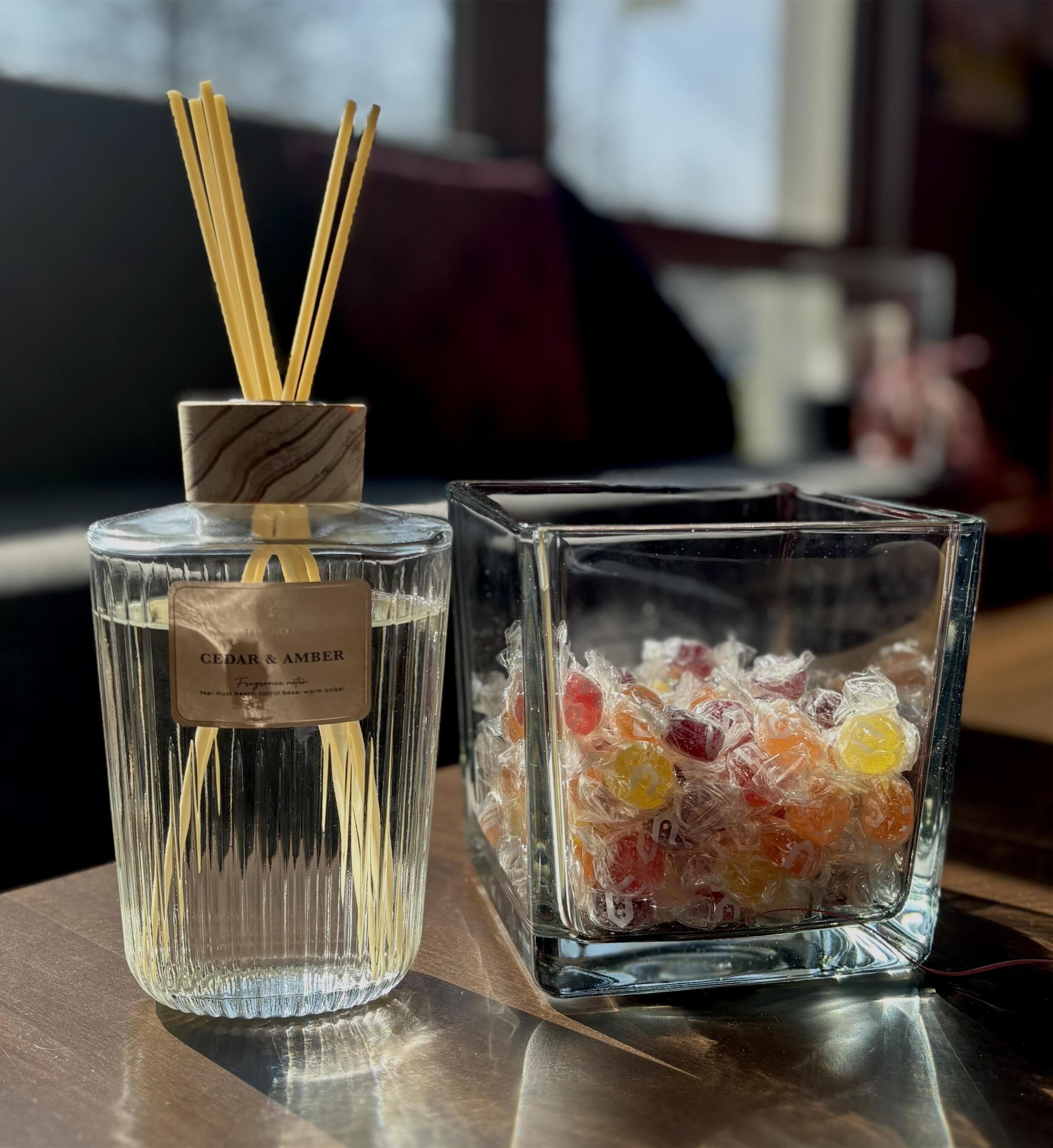 Uma garrafa de vidro com etiqueta e varetas de difusor de aroma, e um recipiente de vidro com balas embaladas.