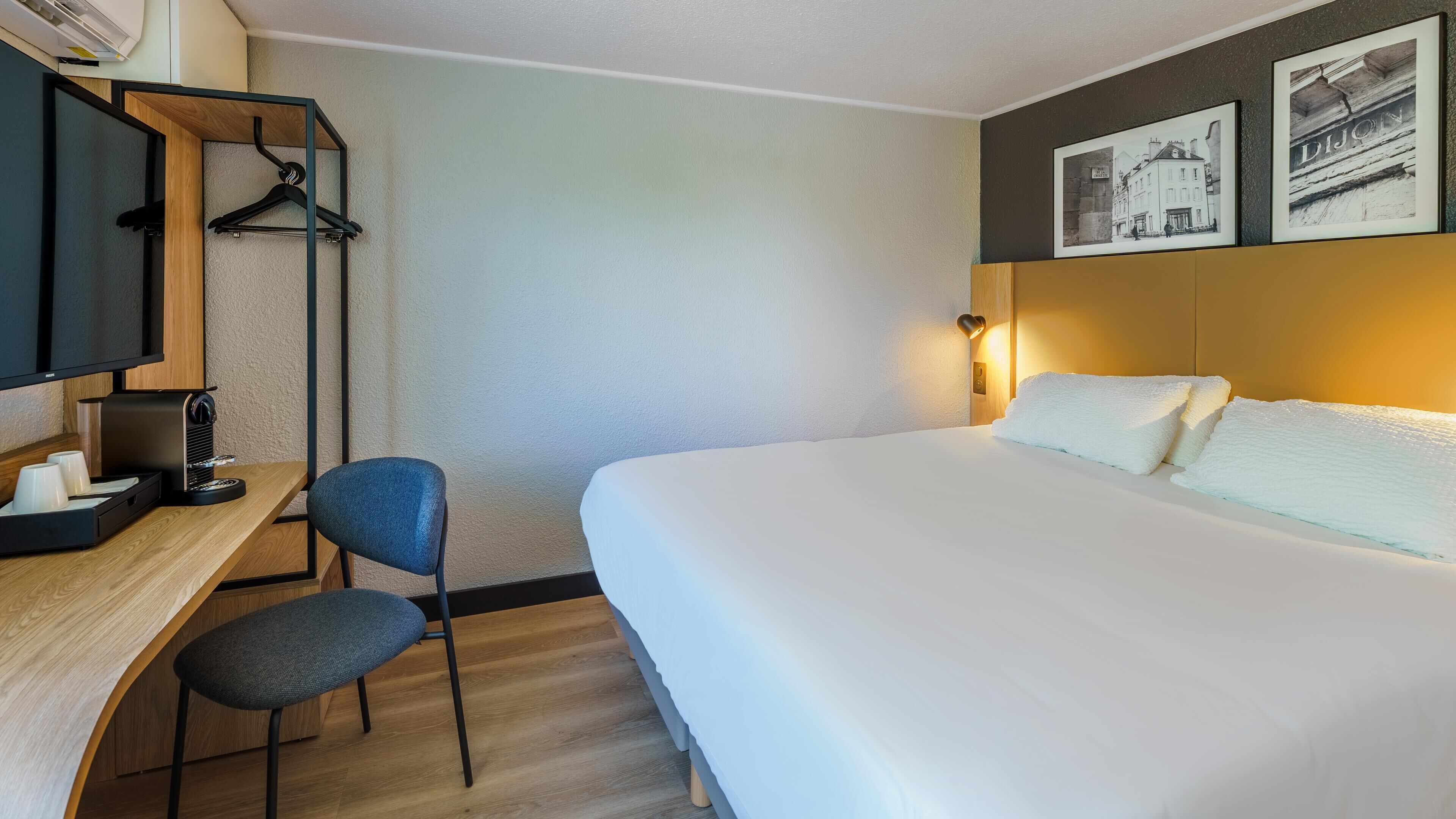 Habitación de hotel con cama, escritorio con silla, televisor y calentador de pared.