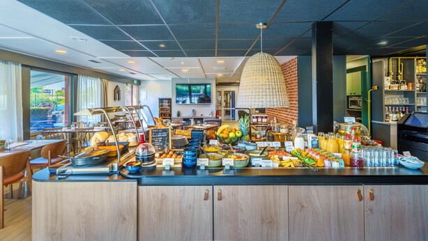 Un bufé de desayuno con diversas opciones de comida y bebidas, una estación de café y vistas al exterior a través de amplios ventanales.