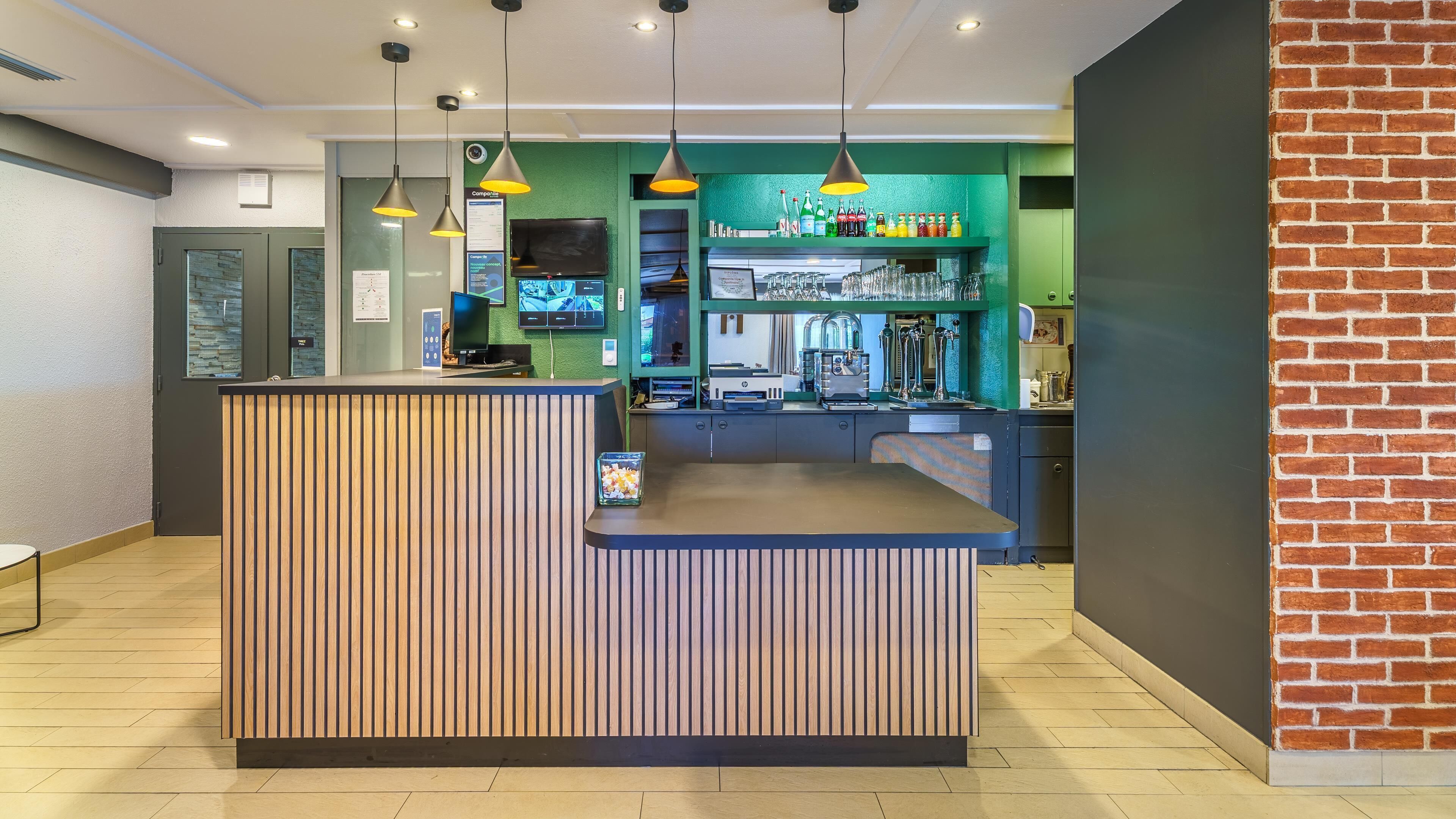 Un espace d’accueil avec un comptoir de réception en bois, un mur végétal agrémenté d’un bar, et un mur en briques servant d’élément décoratif.