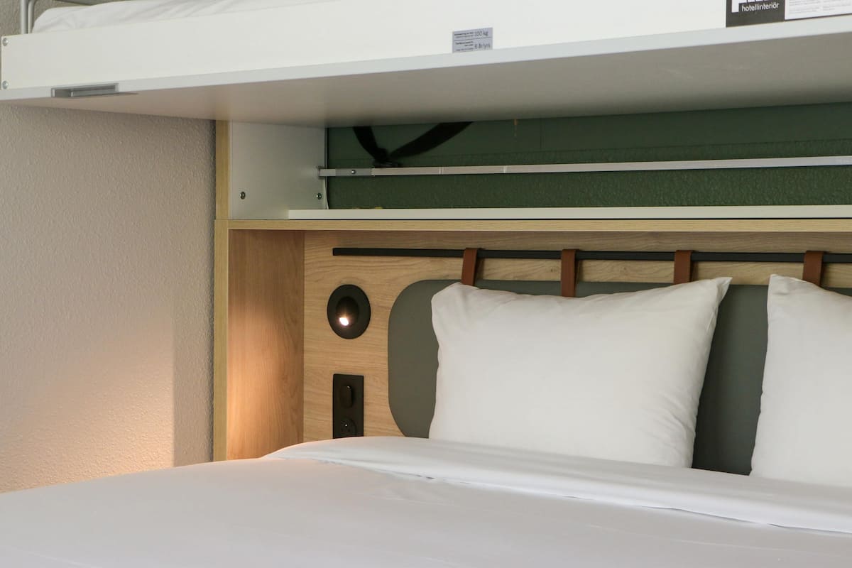 A bunk bed with a wooden headboard, a pull-out desk, and a small shelf above the bed.