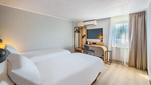 Habitación de hotel con dos camas, un escritorio, una silla, un televisor y un equipo de aire acondicionado.