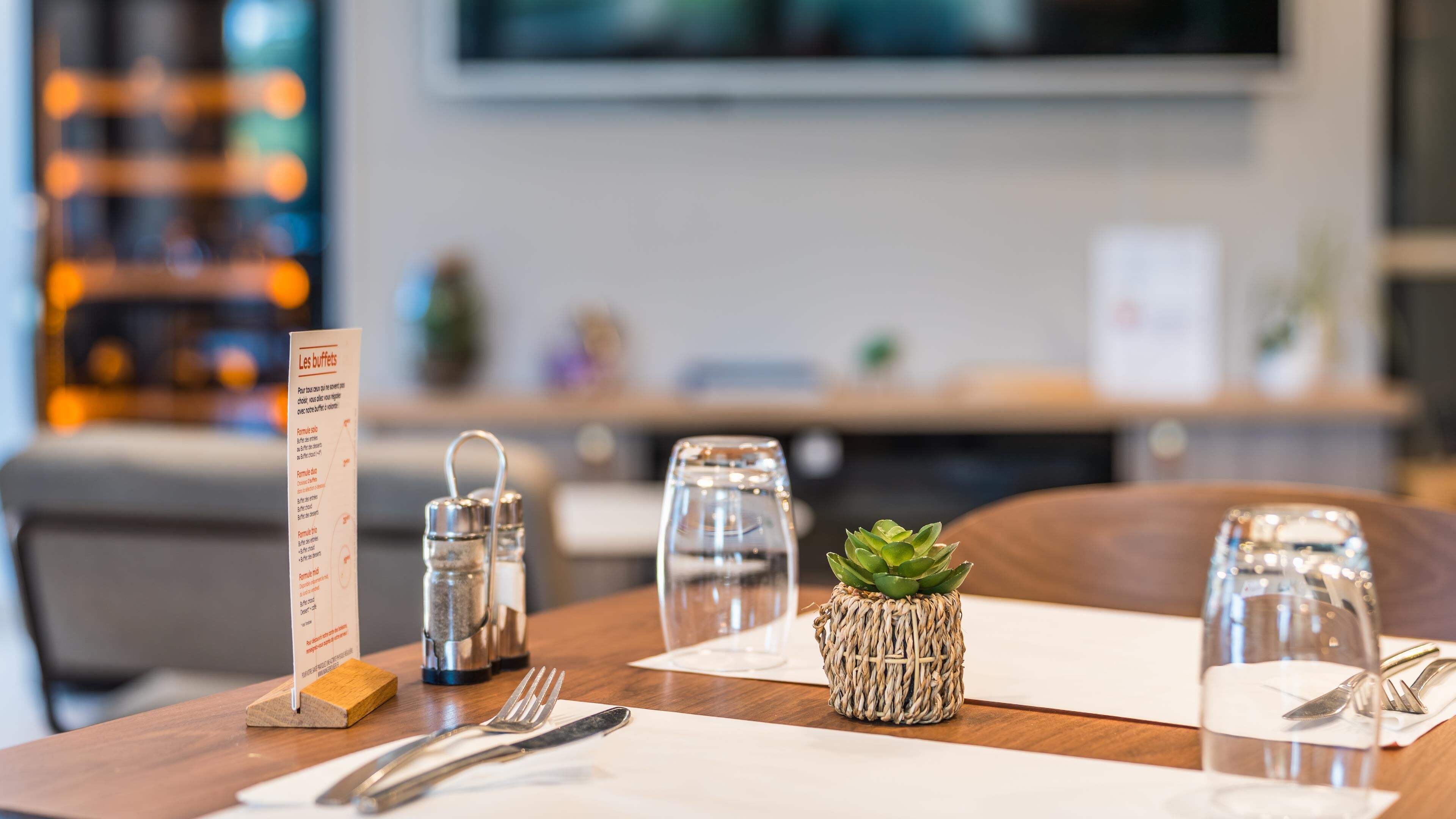A table set with a menu, salt and pepper shakers, a small succulent plant, and a glass of water.