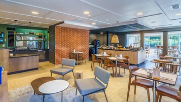 Um café moderno com parede de destaque em tijolo, mesas e cadeiras de madeira, área de bar e vista para o exterior.
