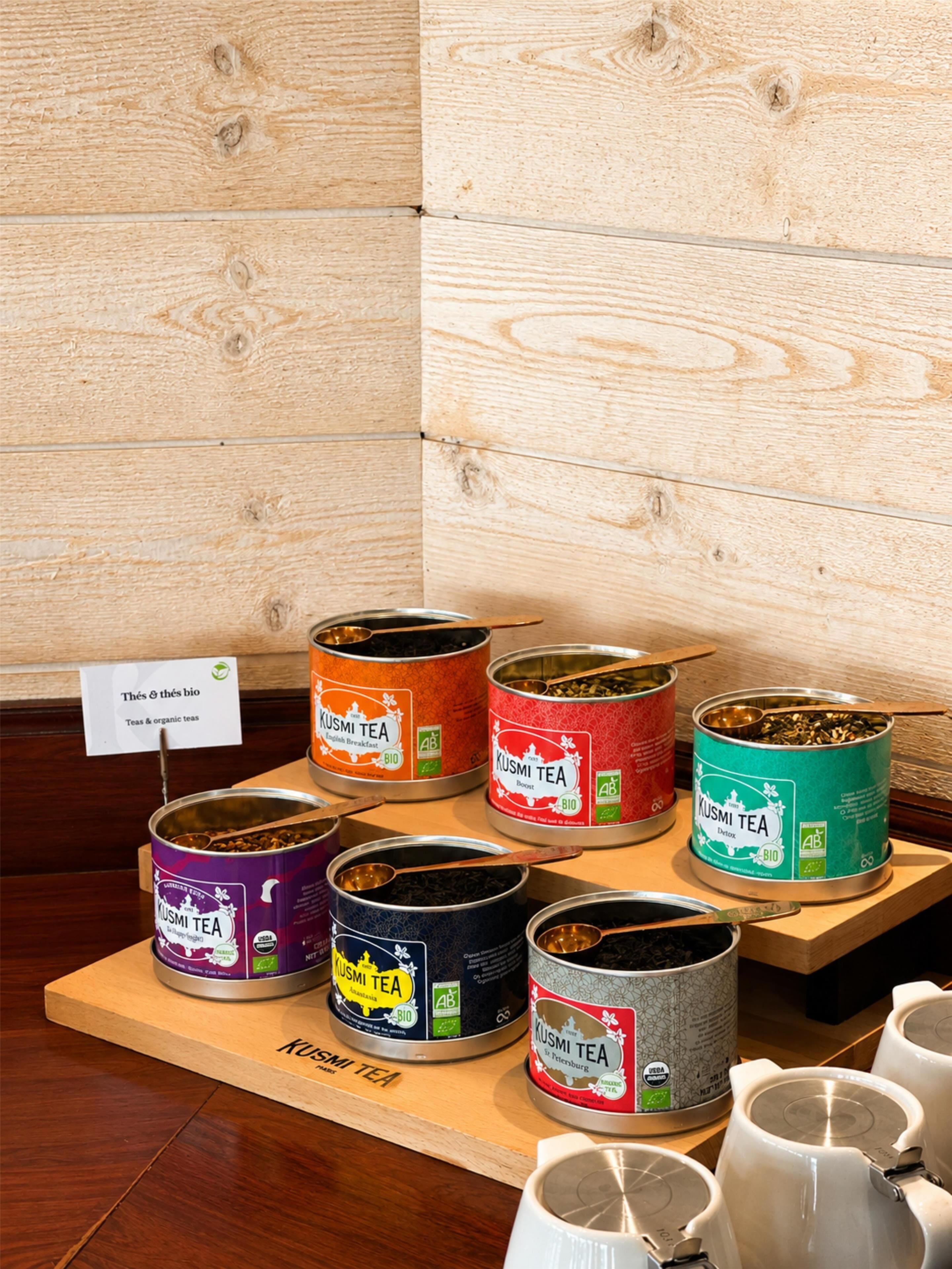 A display of various KUSMI TEA cans on wooden stands.