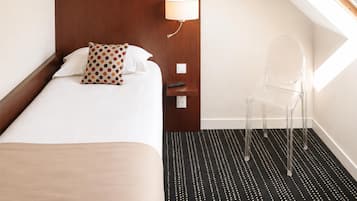 A hotel room with a bed, a nightstand, a lamp, a chair, and a skylight.