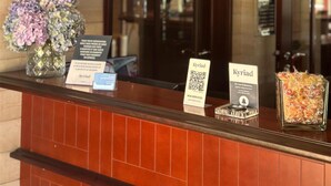 A hotel reception desk with a menu board, a QR code, and a vase of flowers. - Hotel Kyriad Saint-Malo Ouest-Dinard (La Richardais)