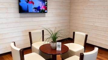 Ein Konferenzraum mit einer Holzwand, einem runden Tisch mit Stühlen, einem Blumentopf und einem an der Wand befestigten Fernseher.