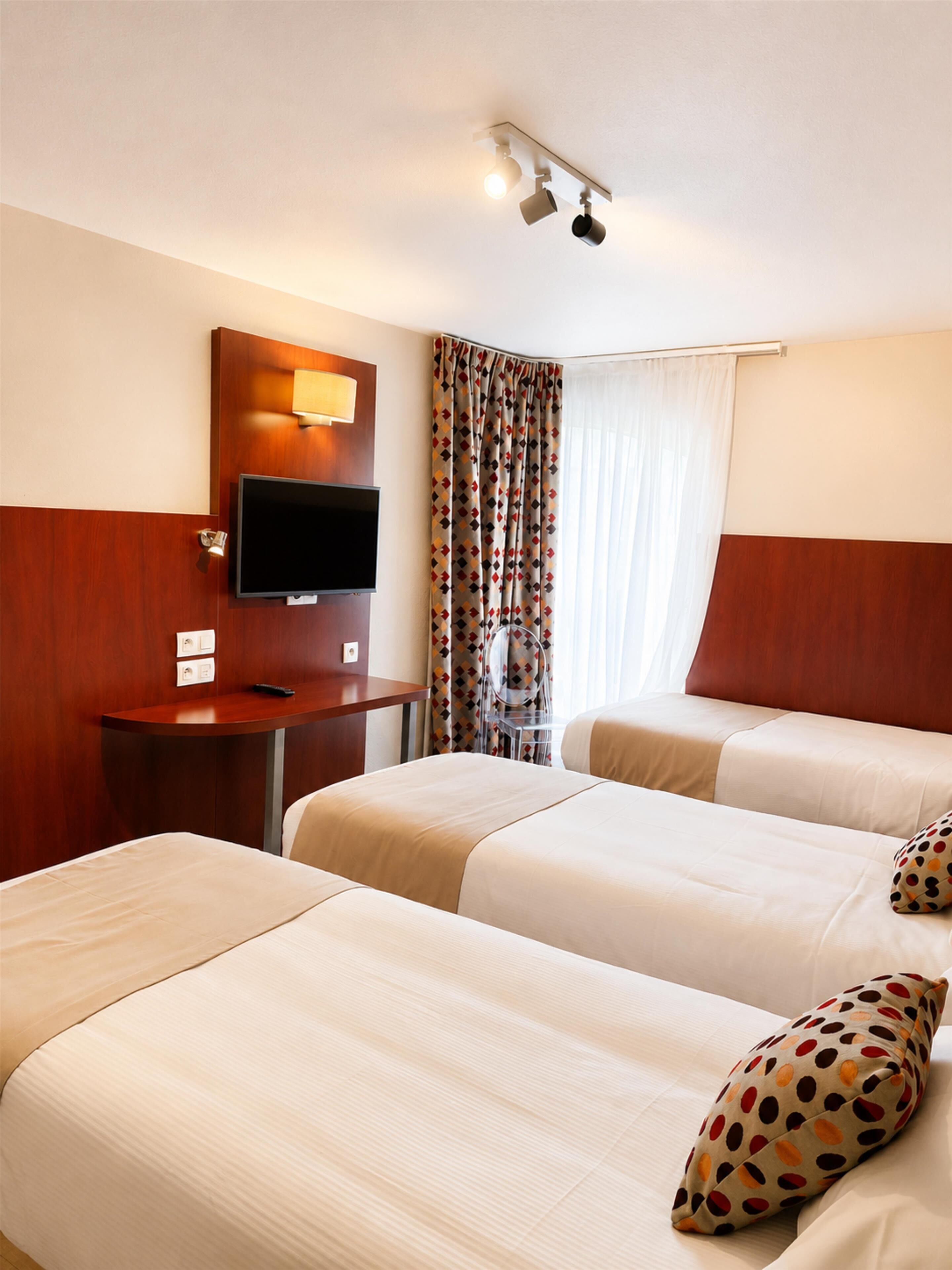 A hotel room with two beds, a TV, a desk, and a window with curtains.