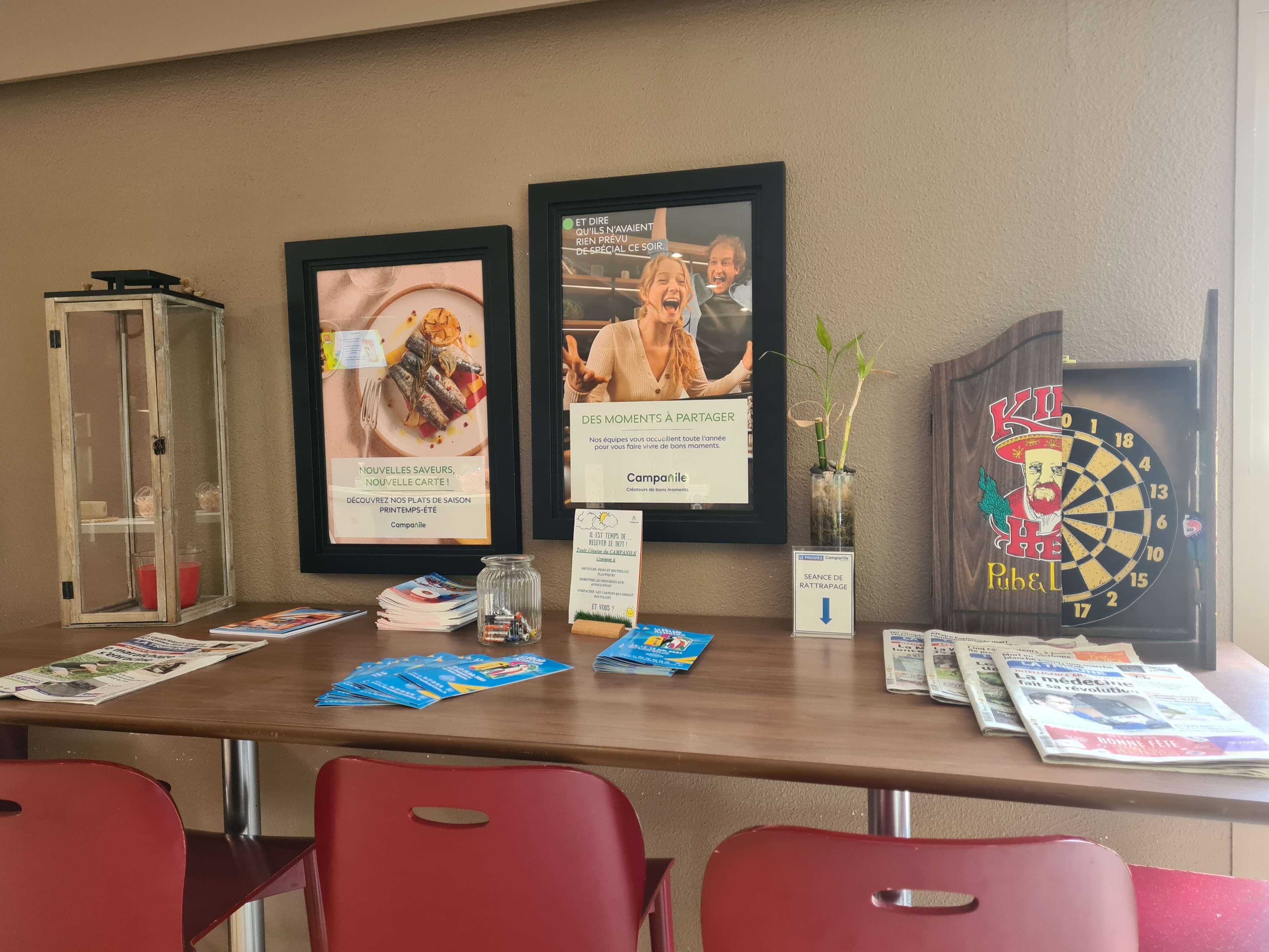 A reception area with framed advertisements, a glass display case, a dartboard, and red chairs.