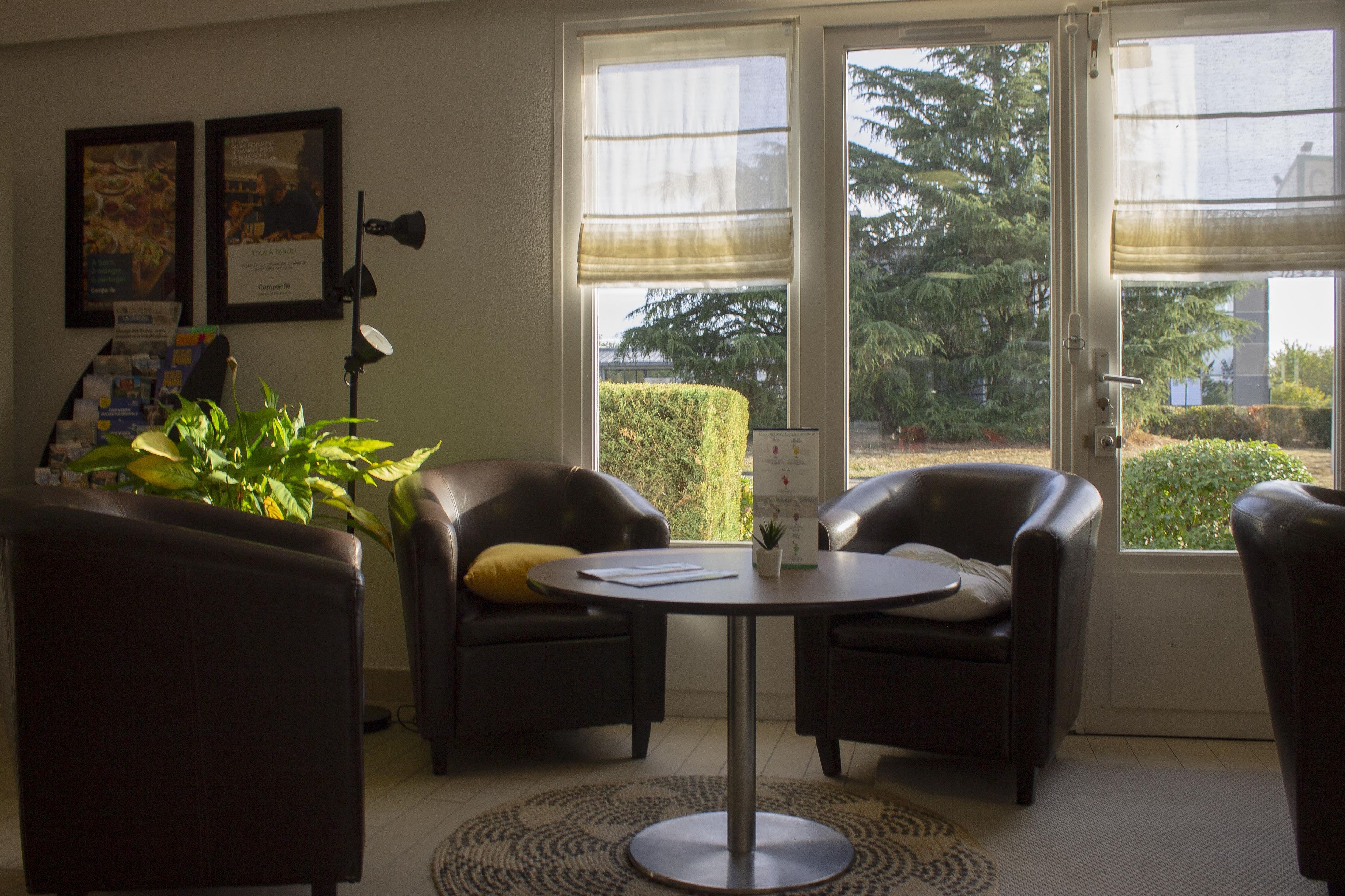 A room with two leather armchairs, a small round table, and a potted plant. There are framed pictures on the wall and a window with a view of trees.