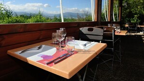 An outdoor dining area with tables set for two, clear skies, and a view of distant mountains. - Hotel Campanile Saint Etienne Est - Saint Chamond (Saint-Chamond)