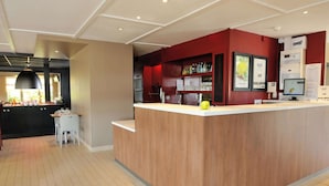 A modern kitchen with a wooden island, a dining area with a white table and chairs, and a red accent wall. - Hotel Campanile Saint Etienne Est - Saint Chamond (Saint-Chamond)