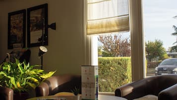 Una habitación con una mesa redonda, dos sillones, una planta en maceta, una ventana con vistas al exterior y una lámpara en el techo.