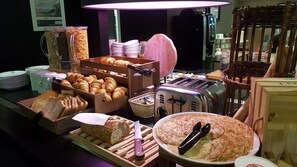 A breakfast buffet with various breads, pastries, and a toaster.