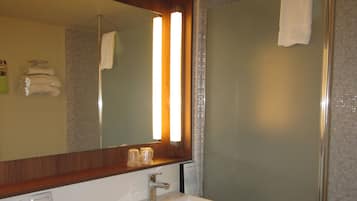 A bathroom with a large mirror, a sink, and a shower.