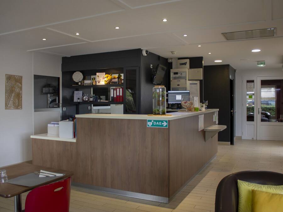 A reception desk with a sign indicating the direction to the DAE room, a computer, and a small plant on the counter.