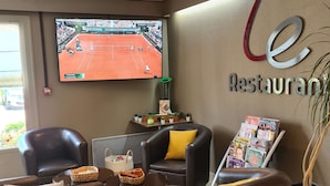 A lounge area with leather armchairs, a coffee table, a TV displaying a tennis match, a magazine rack, and a sign reading "le Restaurant". - Hotel Campanile Saint Etienne Est - Saint Chamond (Saint-Chamond)