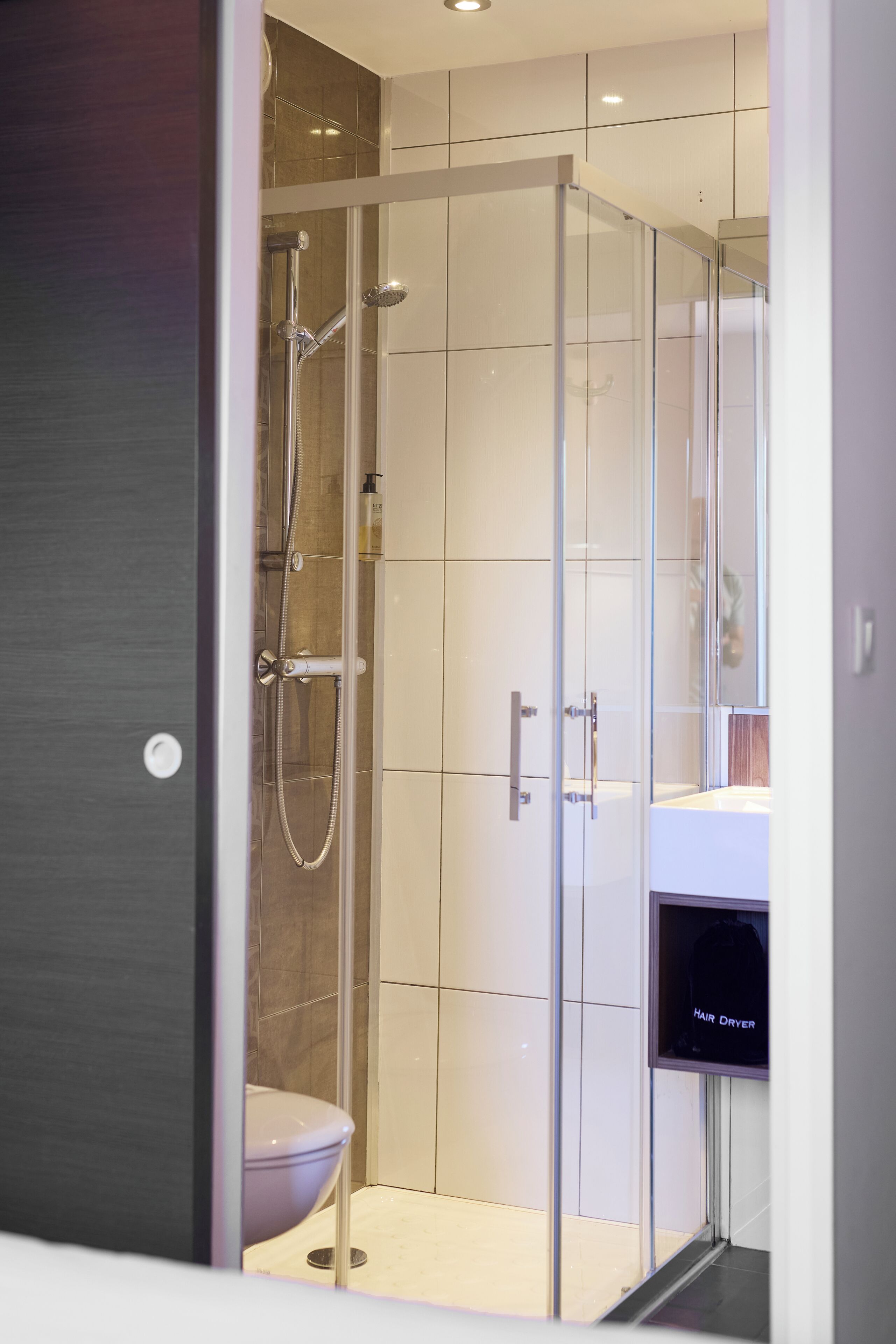Une salle de bain moderne avec une douche à parois de verre, des toilettes et un sèche-cheveux posé sur le comptoir.