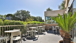 An outdoor patio area with multiple tables and chairs, surrounded by a white fence and lush greenery. - Hôtel Cyano Fréjus-Saint Raphaël (Fréjus)