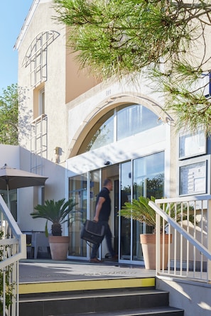 Une entrée d’immeuble avec une porte en verre, un escalier et des plantes en pot.