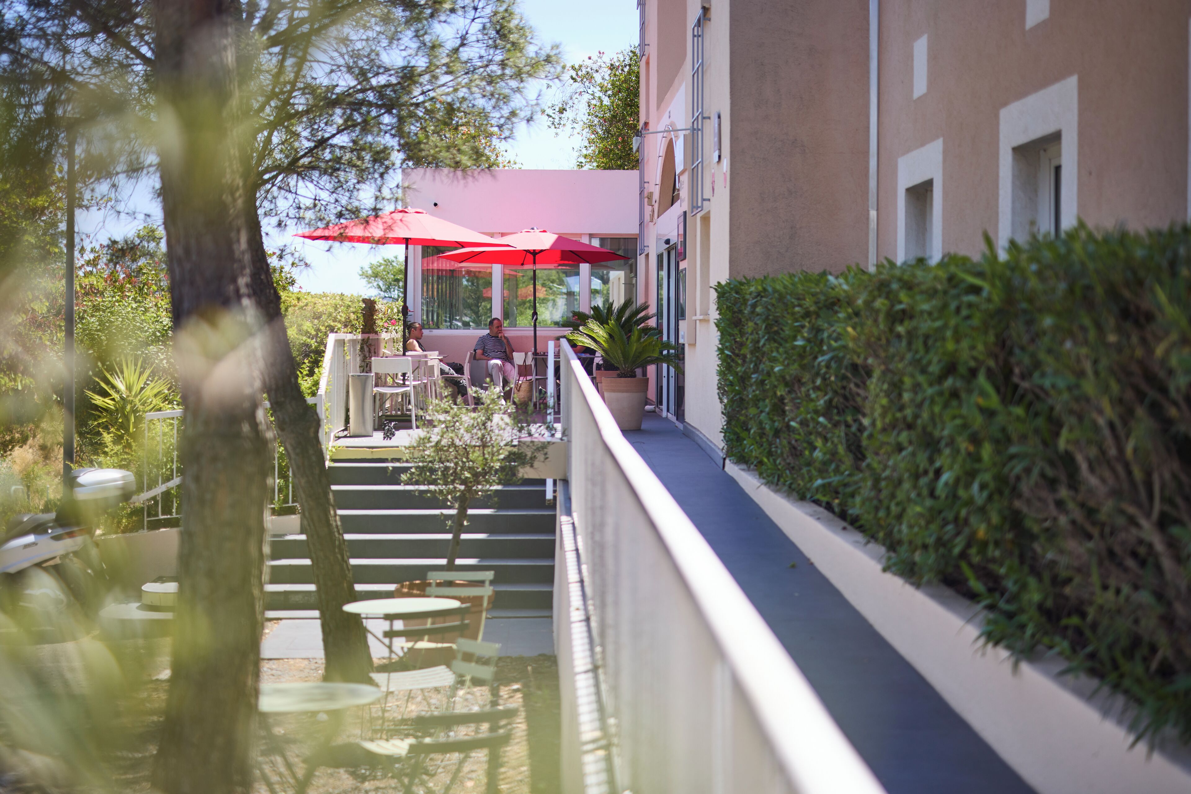 An outdoor seating area with tables and chairs, red umbrellas, and a building with a red roof.