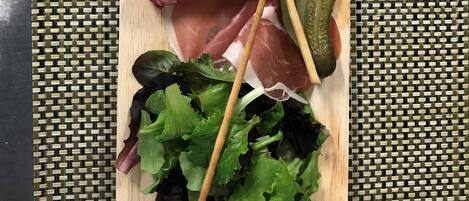 Una tabla de madera con diversos embutidos, encurtidos y verduras de hoja.