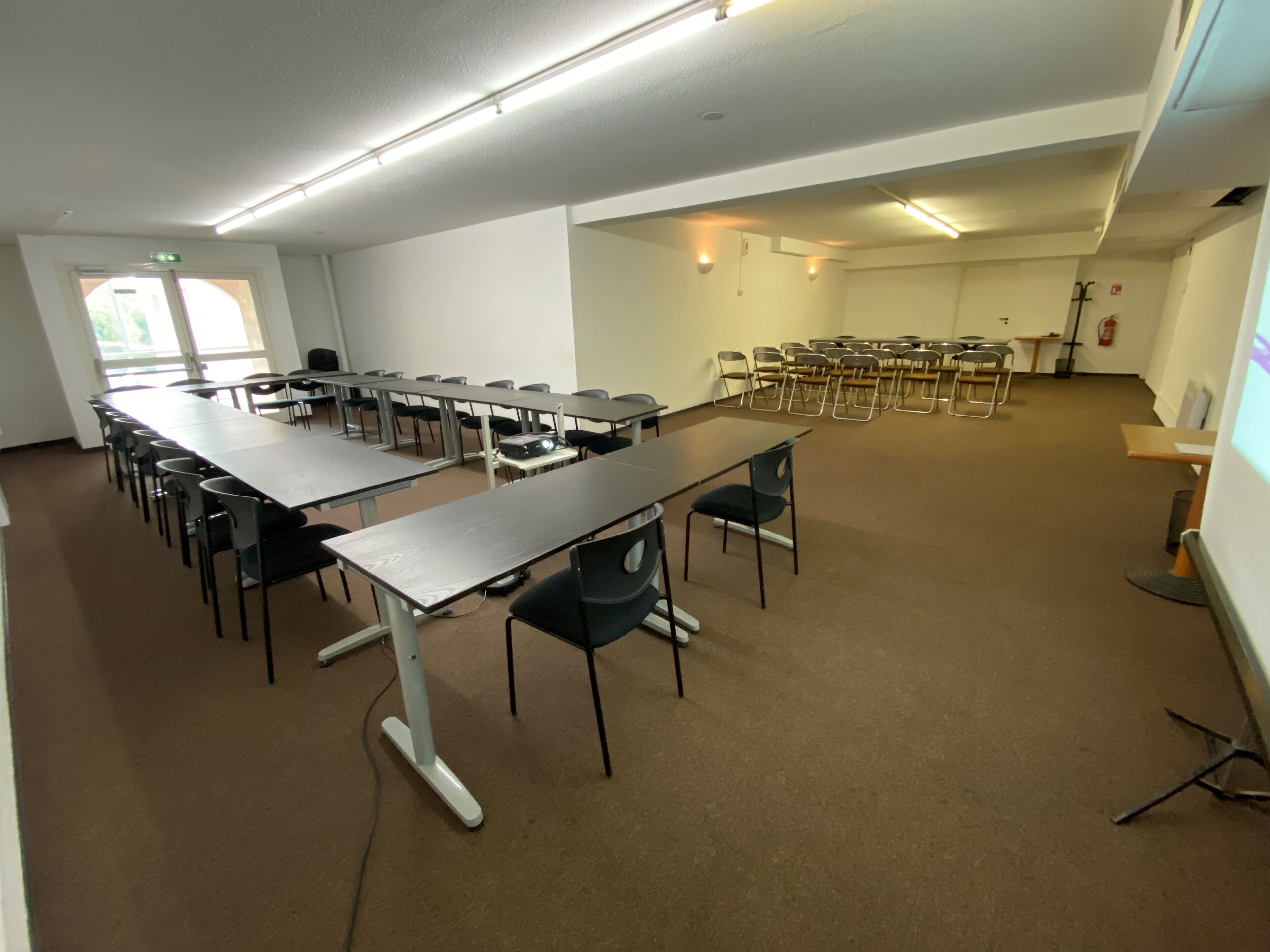 Un salón de conferencias con largas mesas y sillas, un proyector y una pizarra.