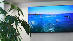 A modern lounge area with a large TV displaying a beach scene, a potted plant, and contemporary seating. - Hôtel Cyano Fréjus-Saint Raphaël (Fréjus)