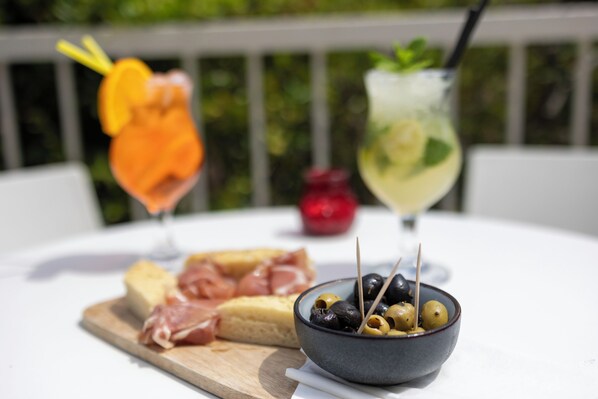 A table with a bowl of olives, a glass of drink with a straw, and a wooden board with cheese and meat.