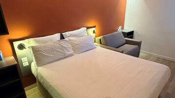 Una cama bien hecha con sábanas blancas, una mesita de noche con lámpara y un aplique de pared.