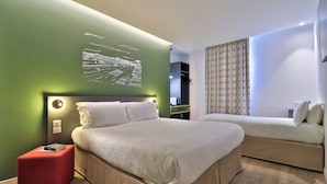 A modern hotel room with a large bed, a smaller sofa, a red ottoman, and a wall-mounted artwork. - Hôtel Cyano Fréjus-Saint Raphaël (Fréjus)