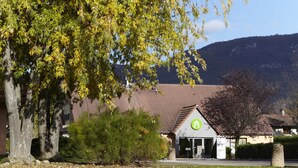 A building with a green logo, surrounded by trees and a mountain in the background. - Hotel Campanile Grenoble Nord - Moirans (Moirans)