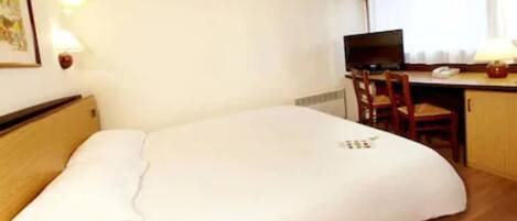 A hotel room with a bed, a desk with a computer, a chair, and a lamp.