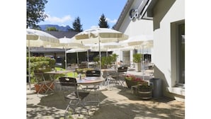 An outdoor patio area with multiple tables and chairs, white umbrellas, and potted plants. - Hotel Campanile Grenoble Nord - Moirans (Moirans)