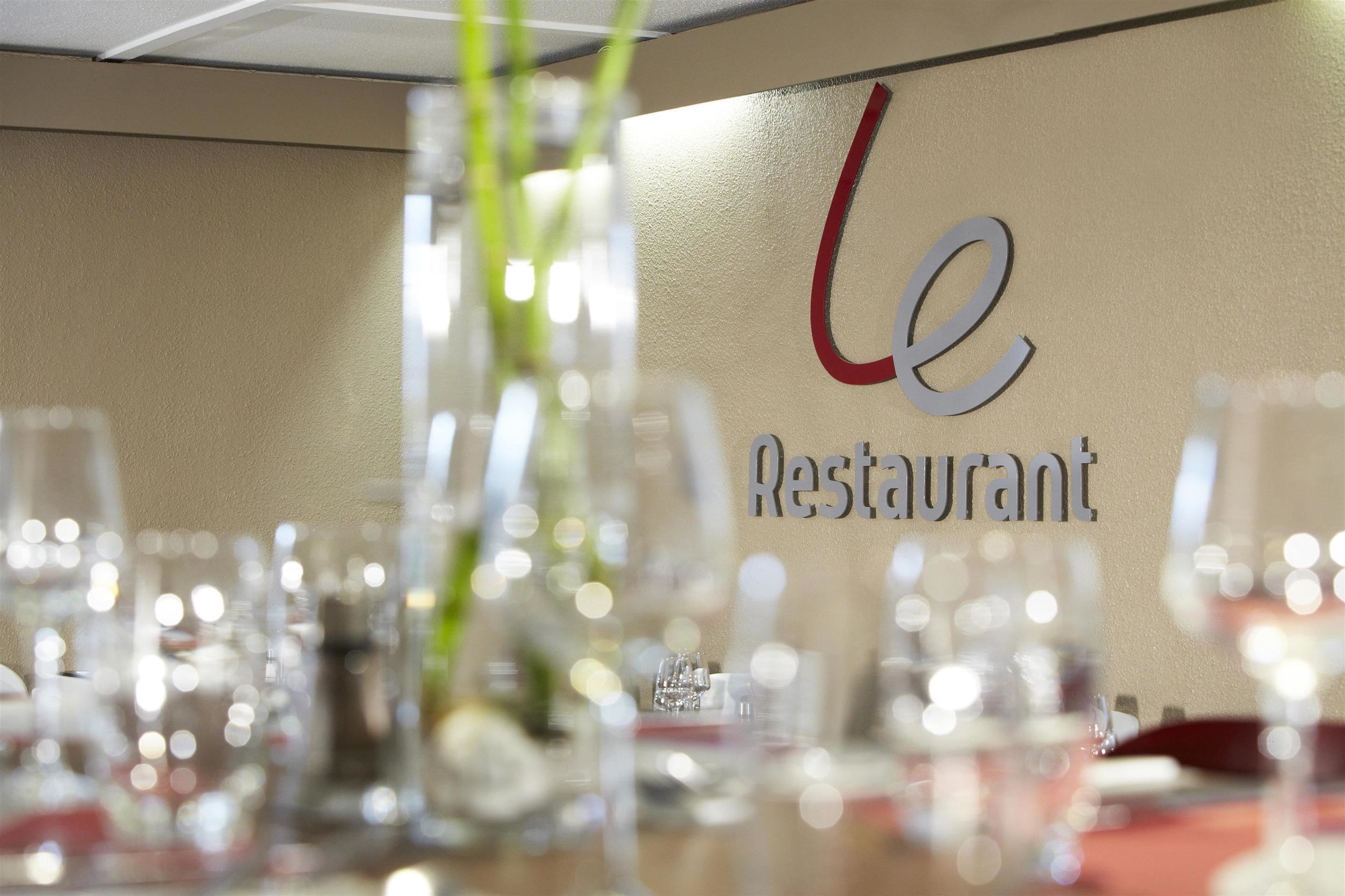 En restauranginteriör med en skylt som visar texten ”le Restaurant” och ett bord dukat med glas och bestick.