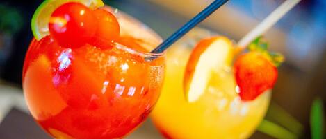 Two fruit-shaped cocktails with straws, garnished with slices of lime and orange.