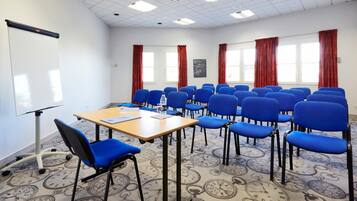 A conference room with a whiteboard, a table with a laptop, and blue chairs arranged around it.