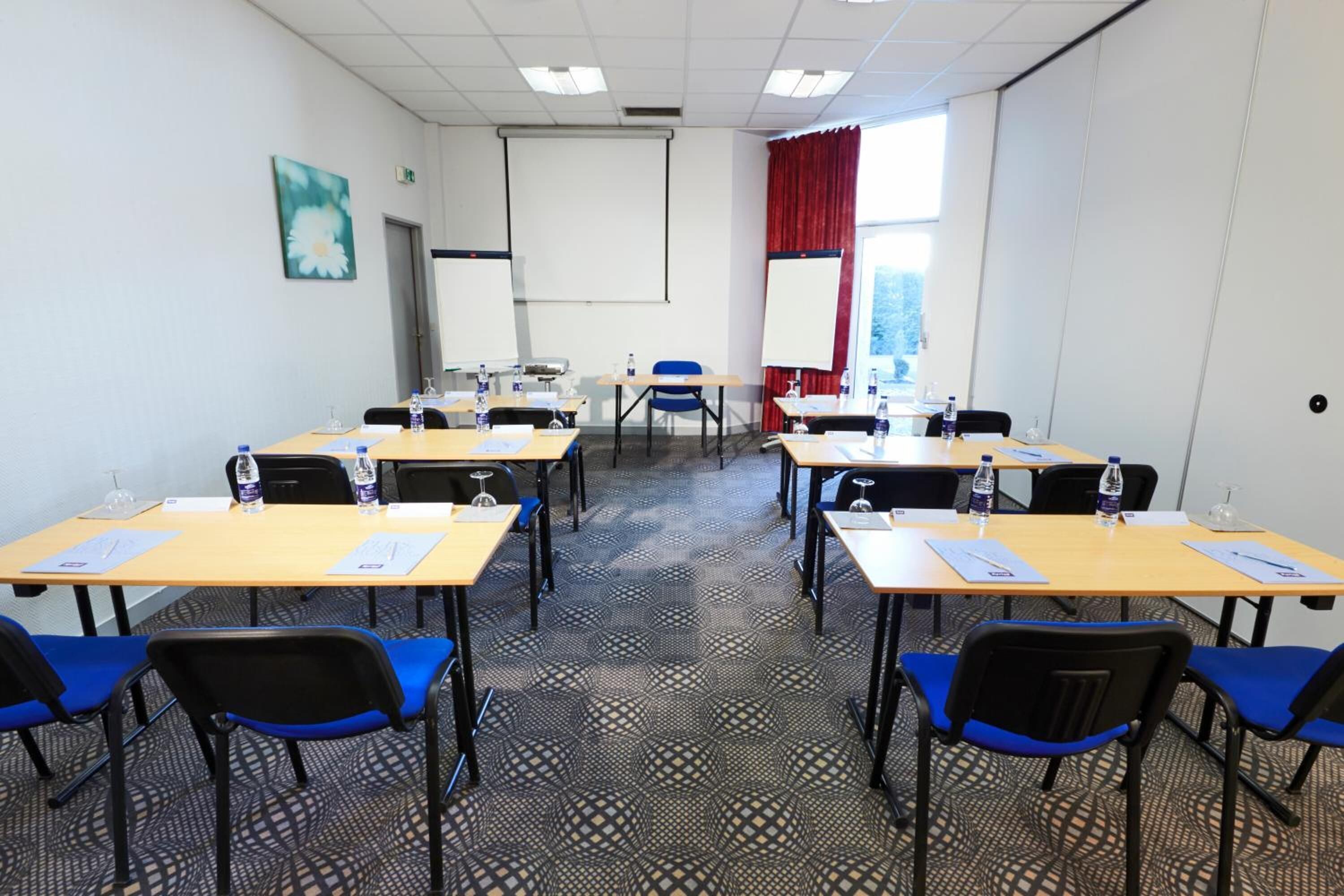Une salle de conférence équipée de plusieurs tables, de chaises bleues et d’un écran de projection.