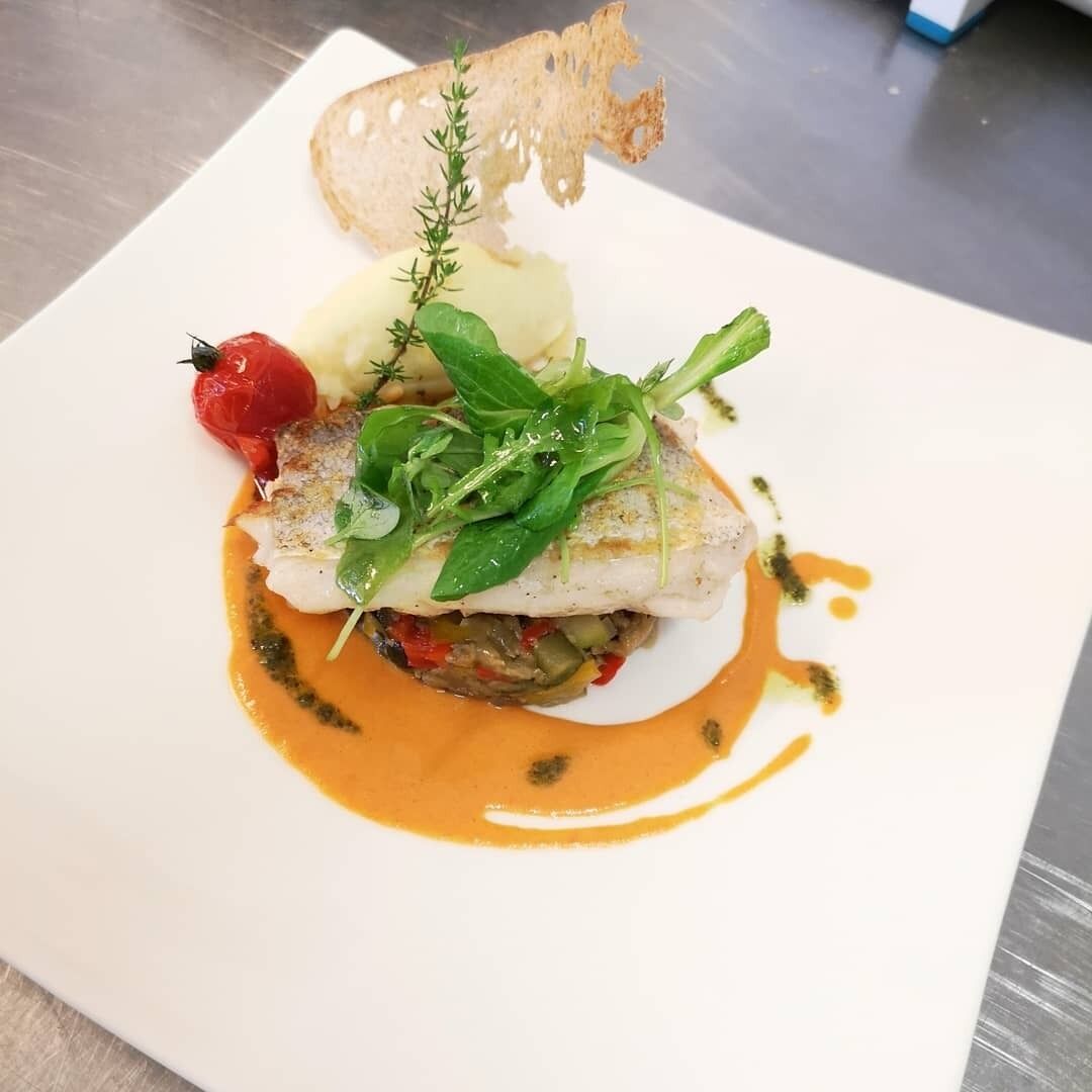 Prato quadrado com filé de peixe, legumes e molho.