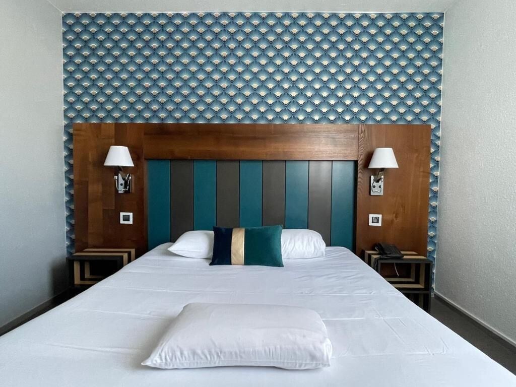 Una habitación de hotel con una cama grande, un cabecero de madera y dos lámparas de noche.