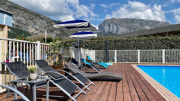 A wooden deck with lounge chairs and umbrellas, a pool, and a mountainous backdrop. - Hôtel le Néron (Fontanil-Cornillon)