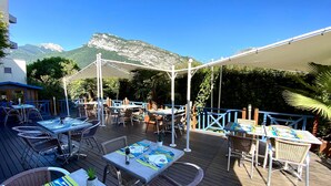 An outdoor patio with tables and chairs, a pergola providing shade, and a mountainous backdrop. - Hôtel le Néron (Fontanil-Cornillon)