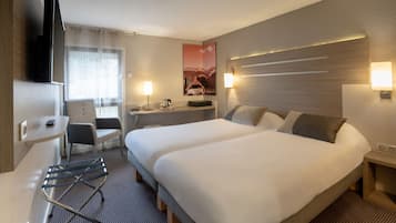 Une chambre d’hôtel avec deux lits, un bureau, une chaise, une télévision et une lampe fixée au mur.