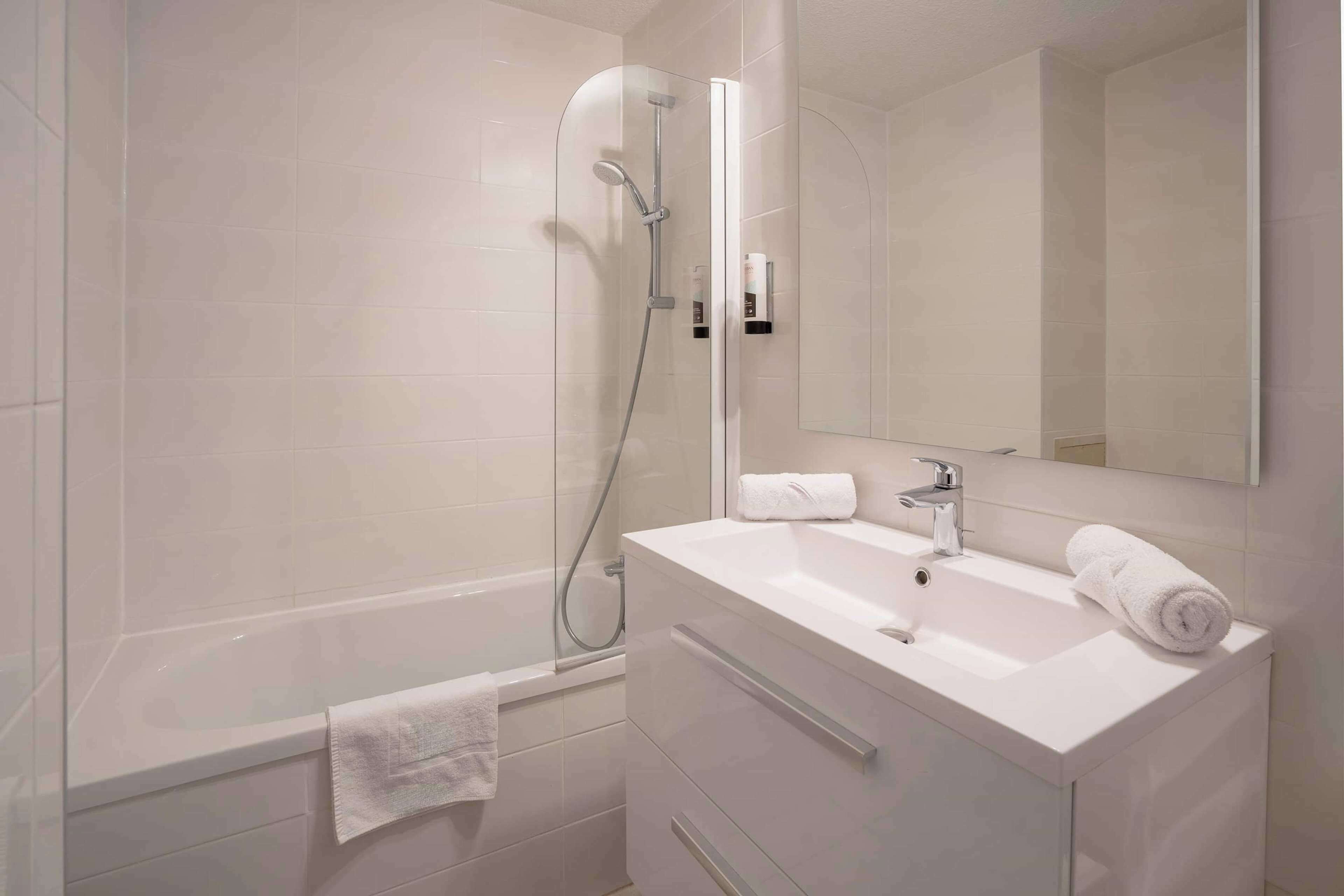 A modern bathroom with a glass-enclosed shower, a white sink with a mirror, and a towel rack.
