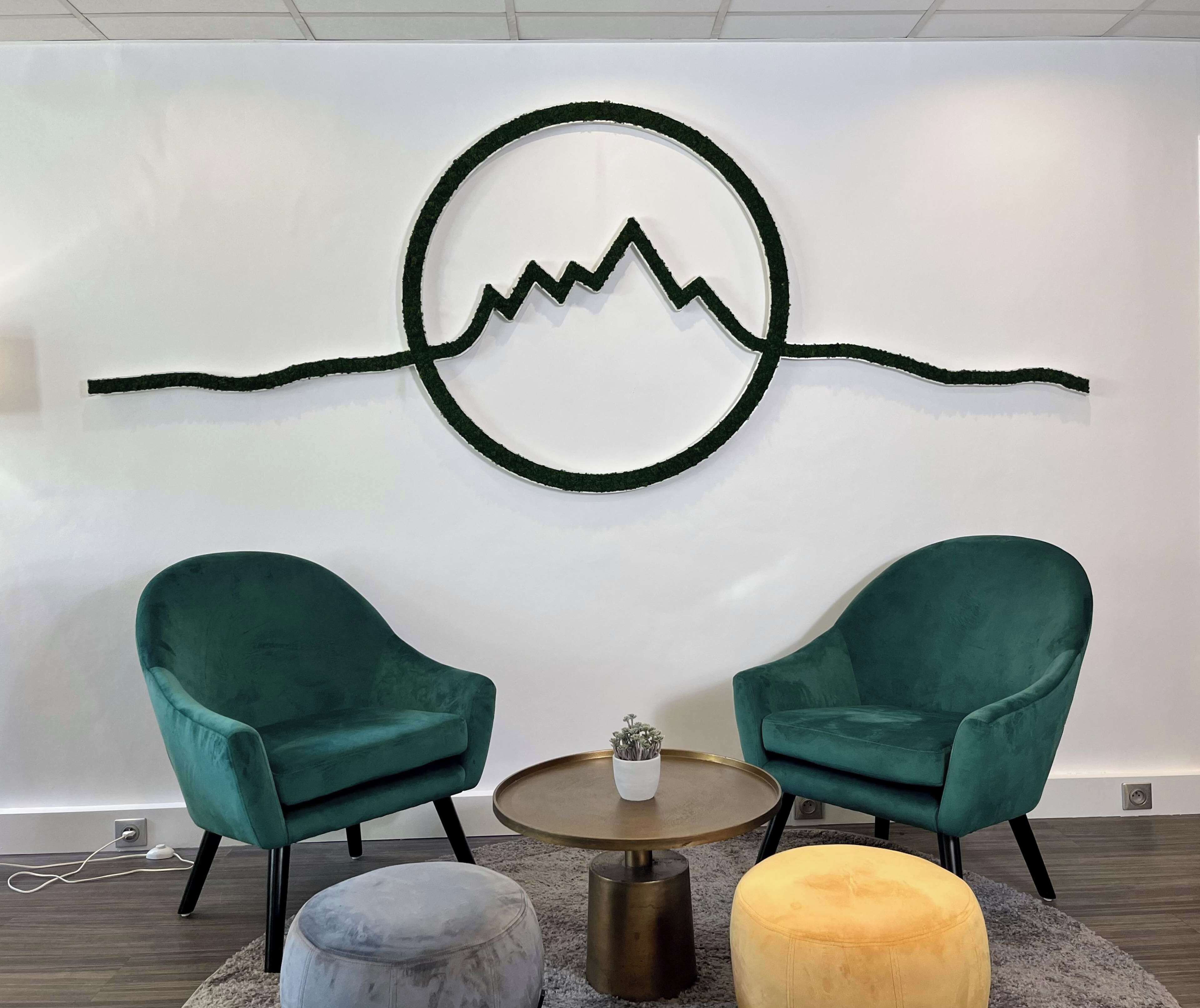A room with two teal armchairs, a small round table with a vase, and a wall-mounted artwork depicting a mountain range.