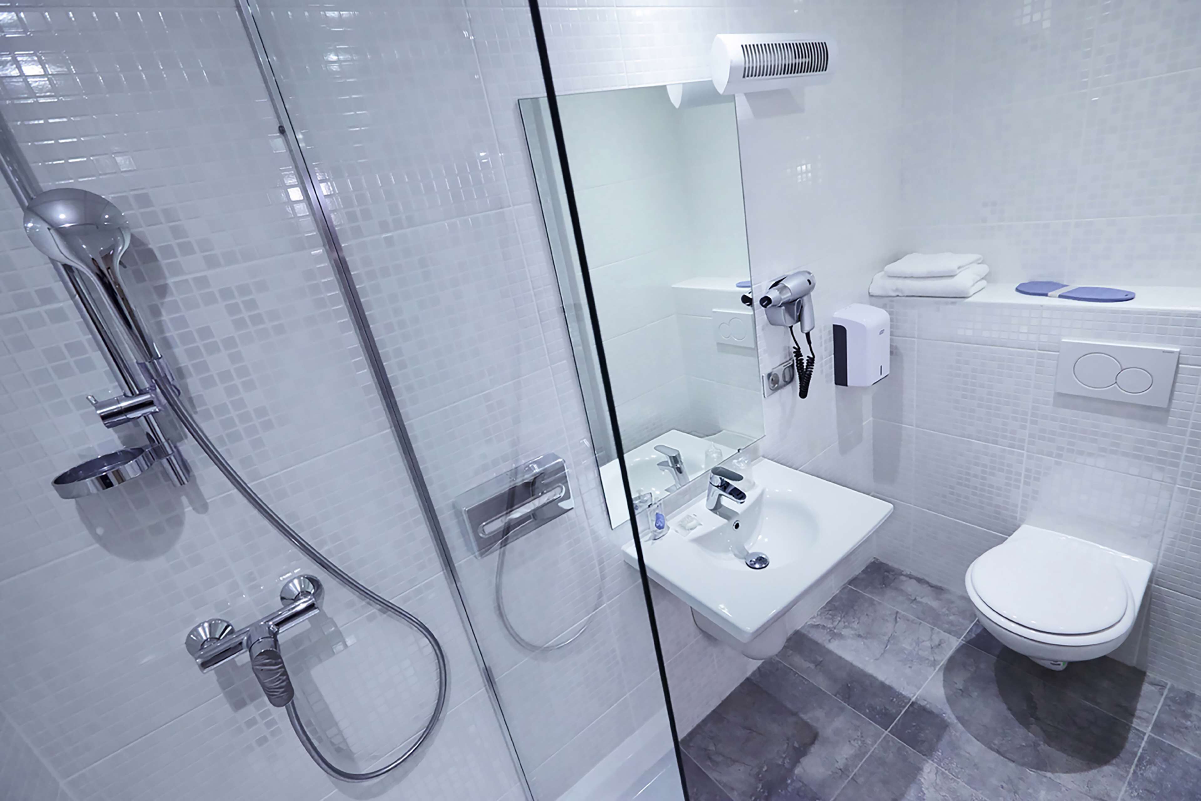 Moderni kylpyhuone, jossa on lasiseinällä varustettu suihku, valkoinen pesuallas ja wc.