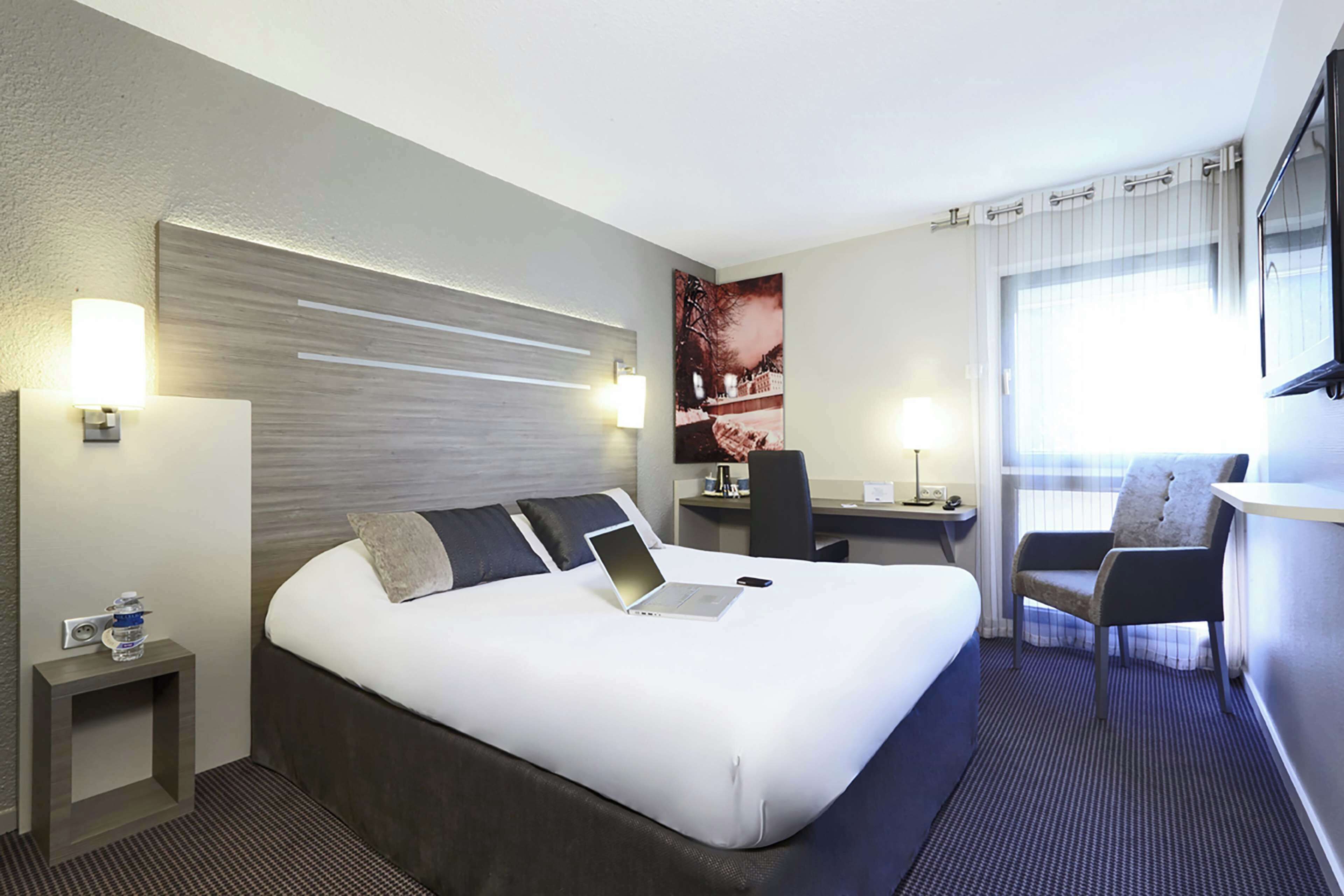 A hotel room with a large bed, a desk with a laptop, a chair, and a TV.